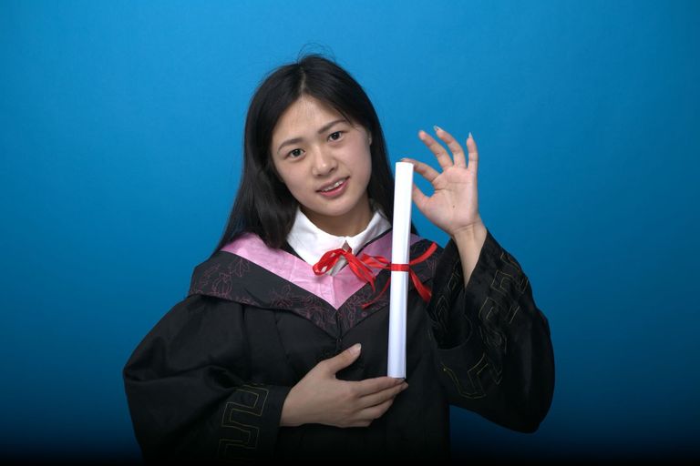 A smiling graduate in cap and gown holds up her diploma.