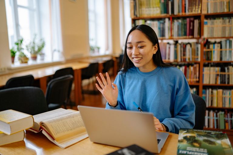 A student waves to her class during an online session in a library.