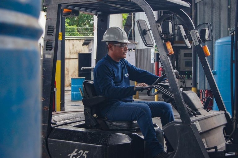 An operator in a hard hat drives a forklift inside a warehouse.