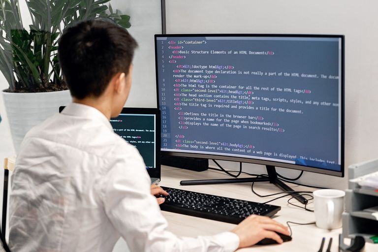 A developer writes code across two monitors.