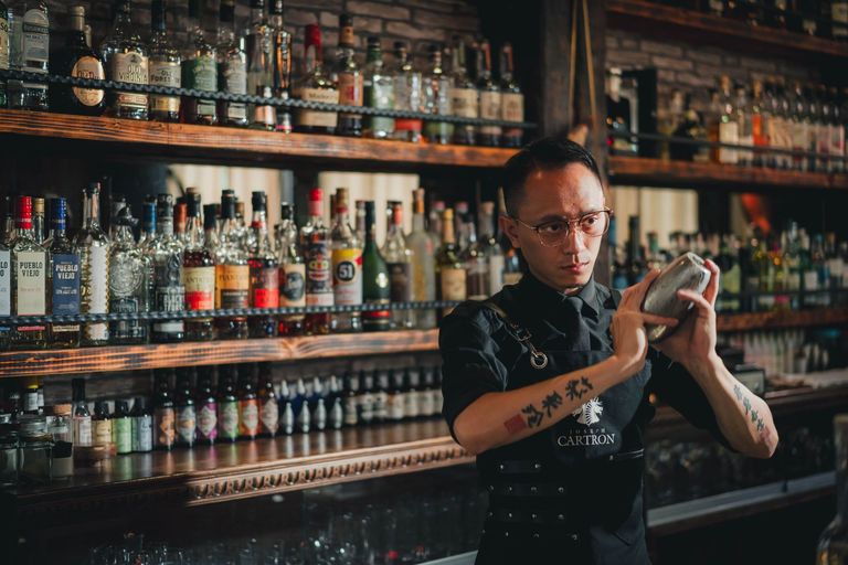 A bartender shakes a cocktail in front of a well-stocked bar.