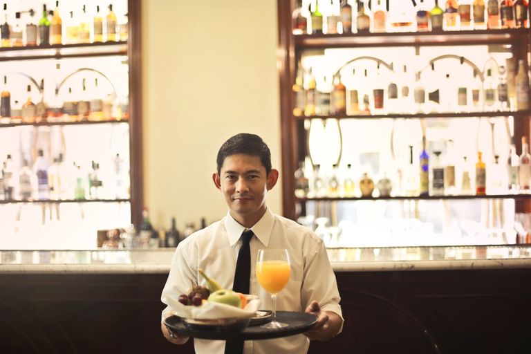 A waiter carries a tray with a drink and a plate.